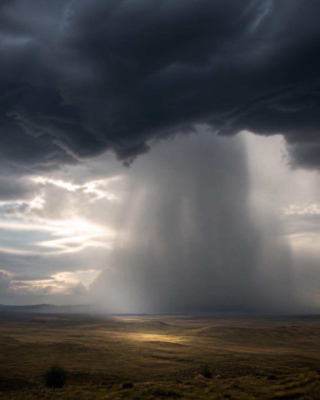 Dramatic rain shaft falling from a dark cloud over a wide open plain
